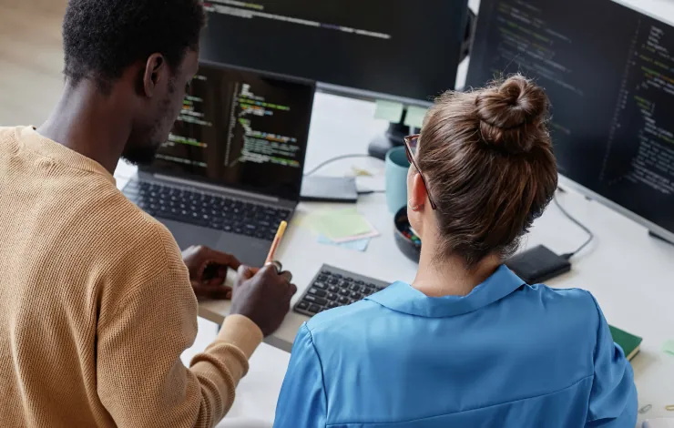 Dois estagiários programando juntos diante de monitores com código